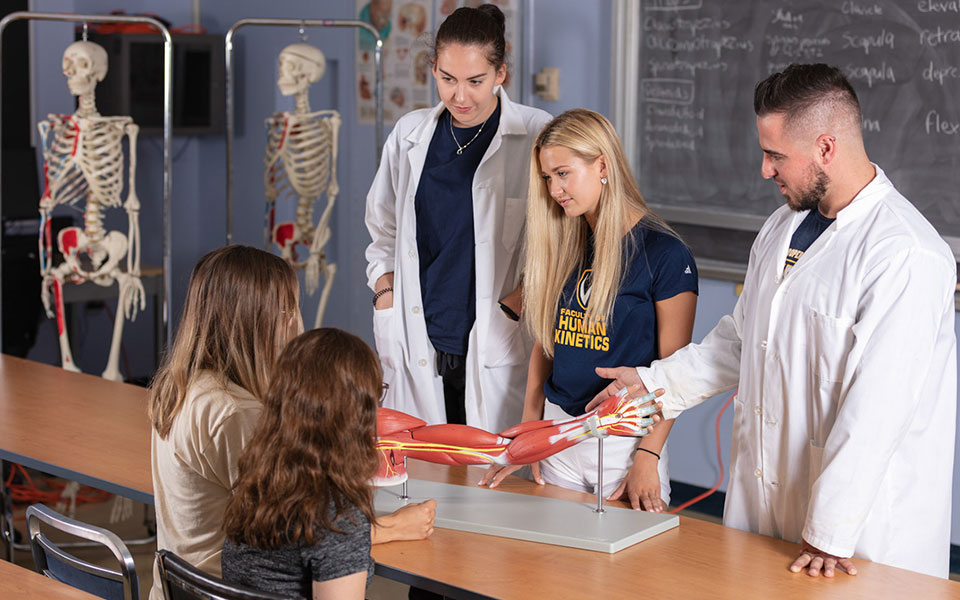 Three kinesiology students showing muscle tissue to kids in a classroom